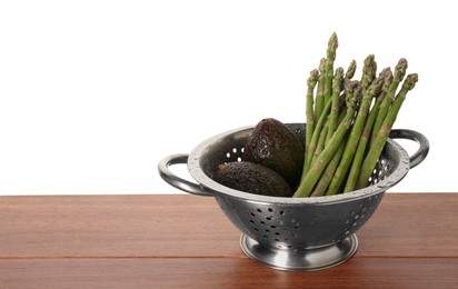 Photo of Metal colander with asparagus and avocados on wooden table against white background, space for text