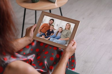 Woman holding frame with photo portrait of her family indoors, closeup