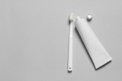 Plastic toothbrush with paste and tube on grey background, flat lay. Space for text
