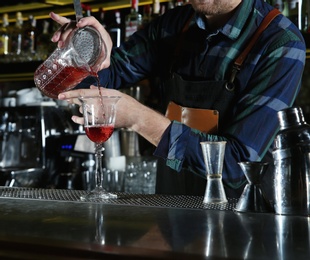 Barman pouring cocktail through strainer into glass at counter in pub, closeup