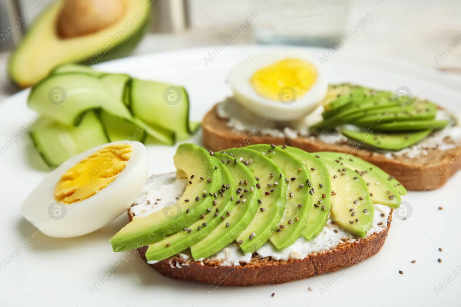 Photo of Crisp rye toast with avocado, cream cheese and quail egg on plate, closeup