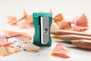 Photo of Green sharpener, colorful pencils and shavings on white wooden table, closeup