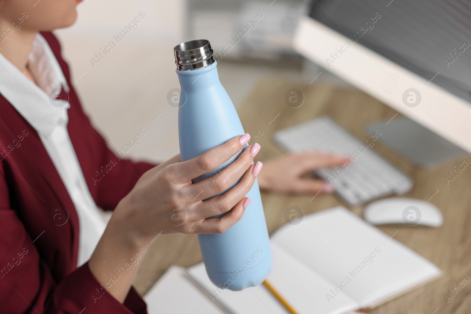 Photo of Woman holding thermos bottle at workplace, closeup.
