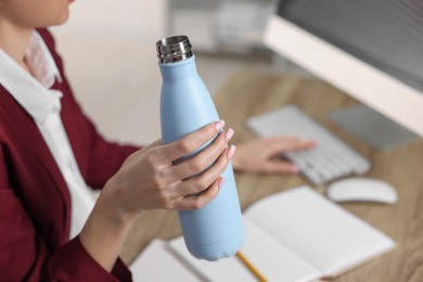 Photo of Woman holding thermos bottle at workplace, closeup.