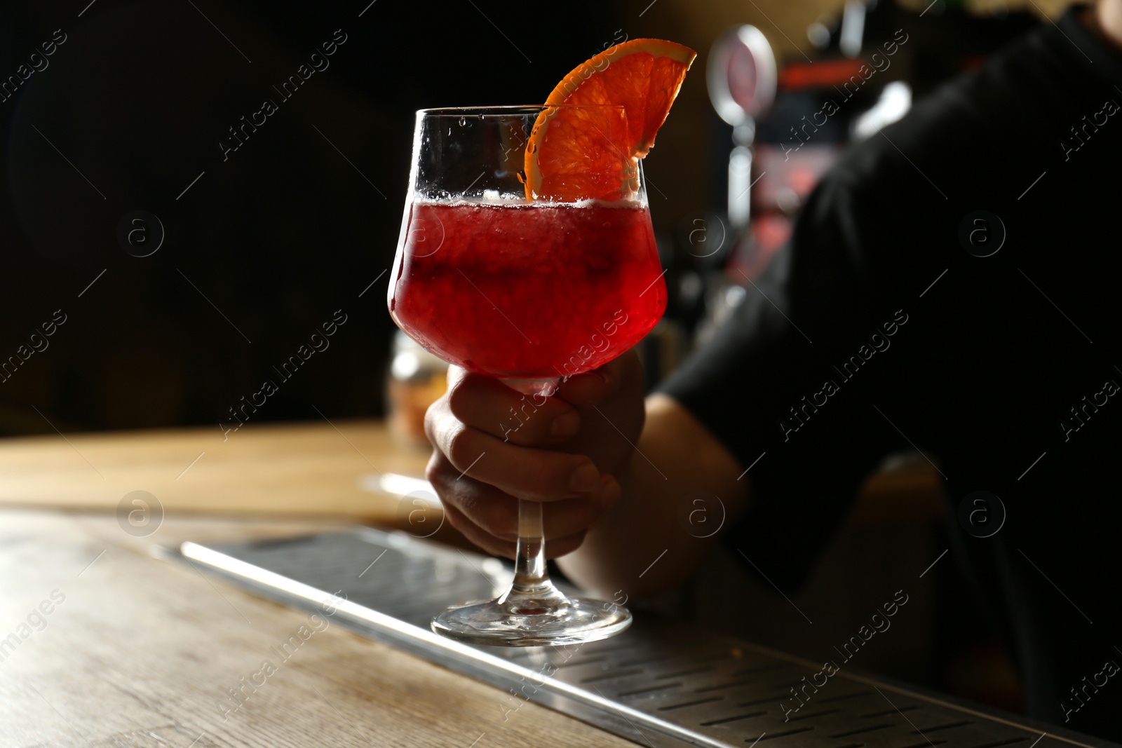 Photo of Bartender holding glass of fresh alcoholic cocktail in bar, closeup