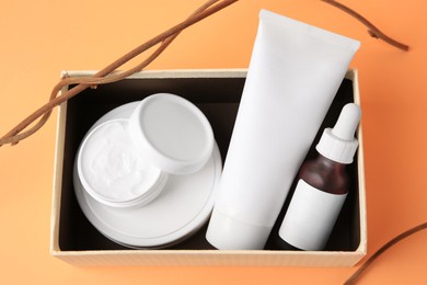 Box with cosmetic products and decorative twigs on orange background, above view