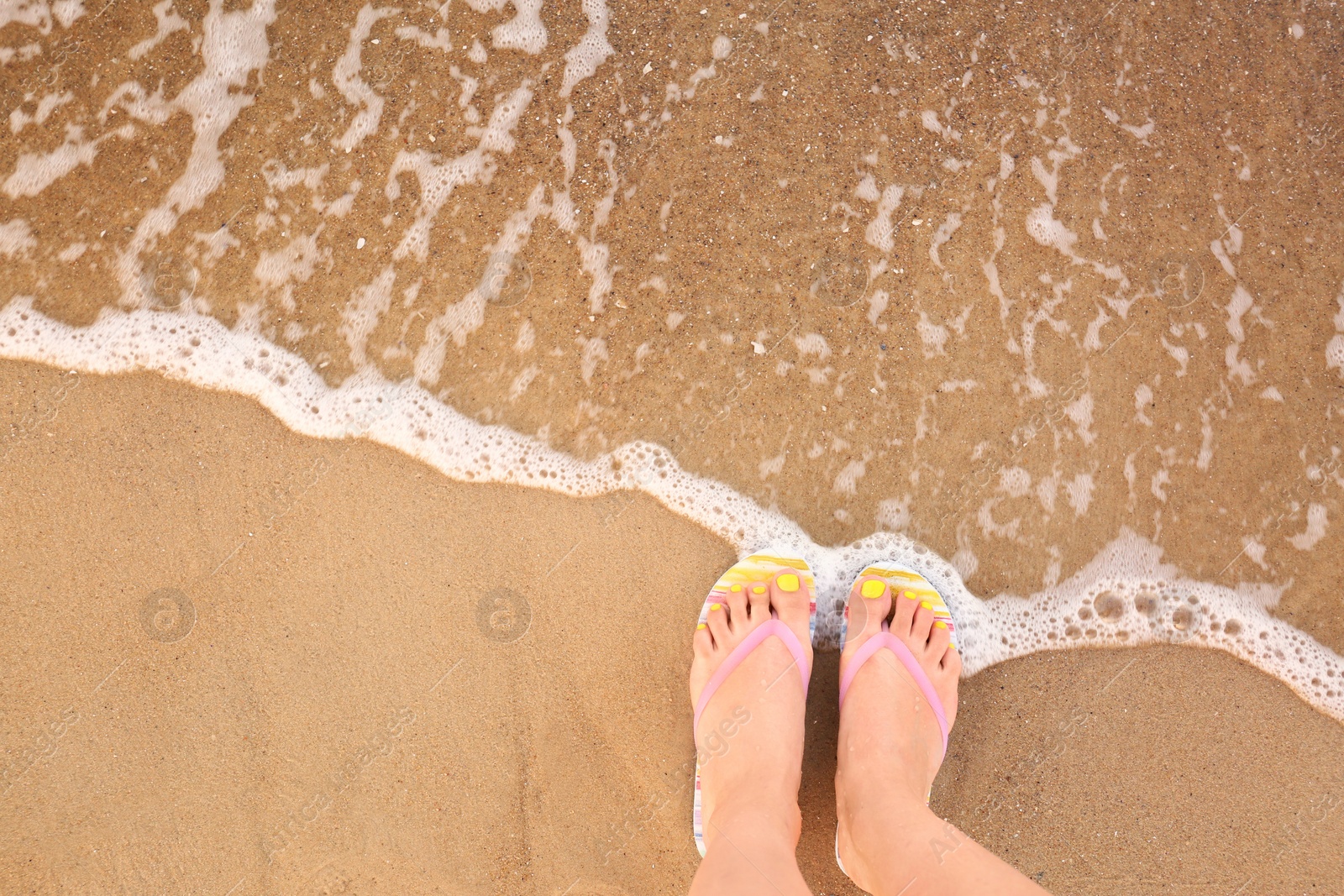 Photo of Top view of woman with stylish flip flops on sand near sea, space for text. Beach accessories