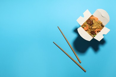 Photo of Box of wok noodles with seafood and chopsticks on turquoise background, flat lay. Space for text