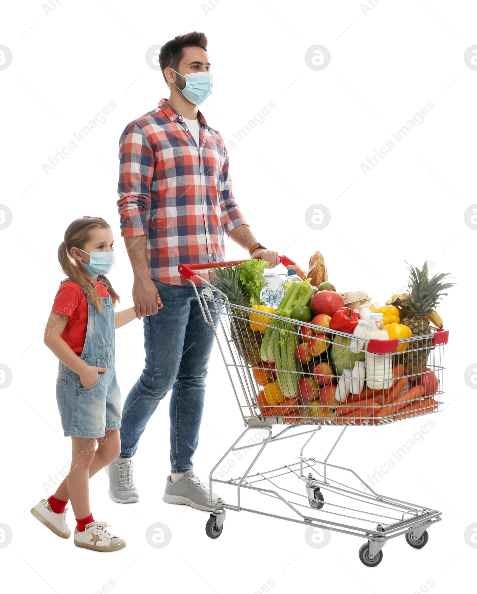 Photo of Father and daughter in medical masks with shopping cart full of groceries on white background