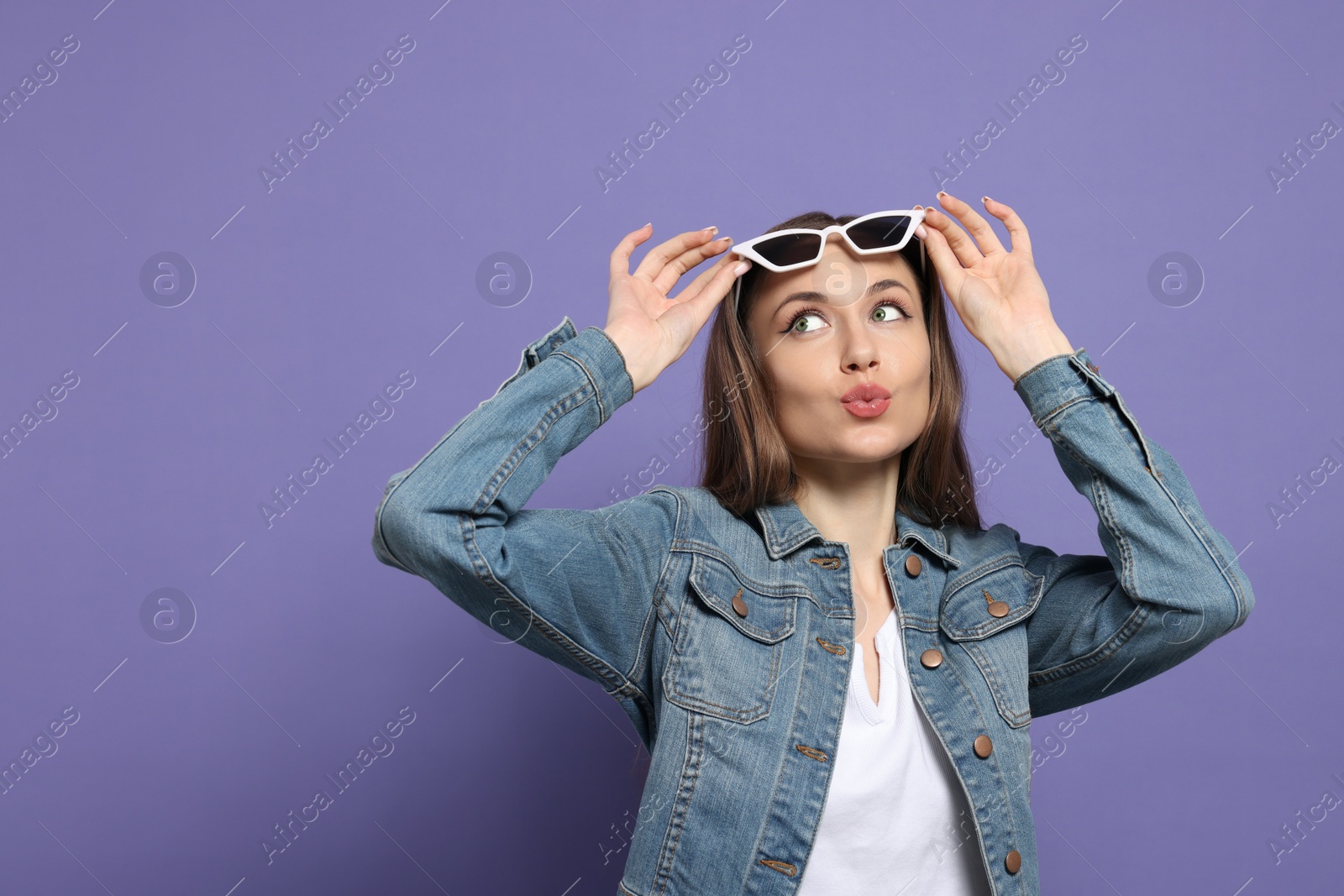 Photo of Beautiful young woman with sunglasses blowing kiss on purple background, space for text