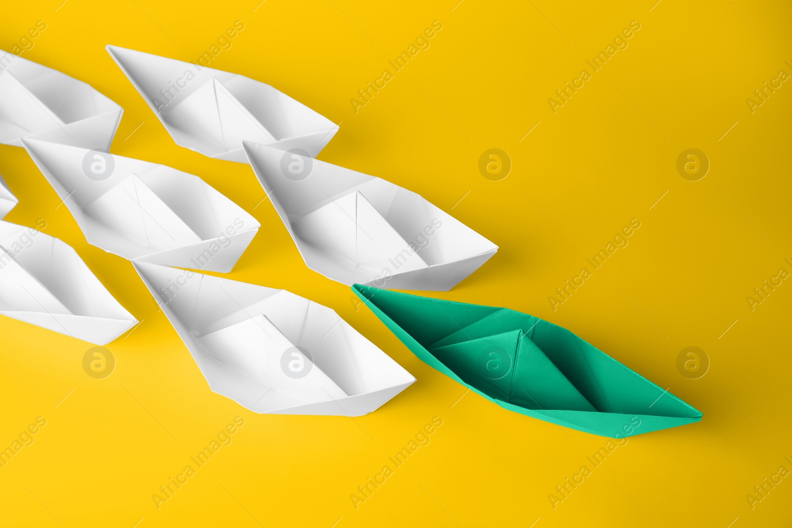 Photo of Group of paper boats following green one on yellow background. Leadership concept