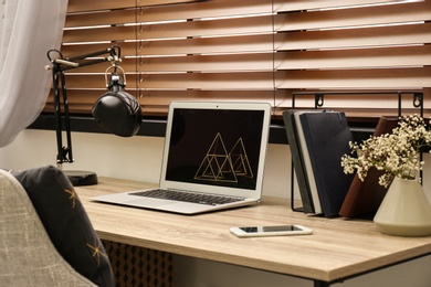 Comfortable workplace near window with horizontal wooden blinds