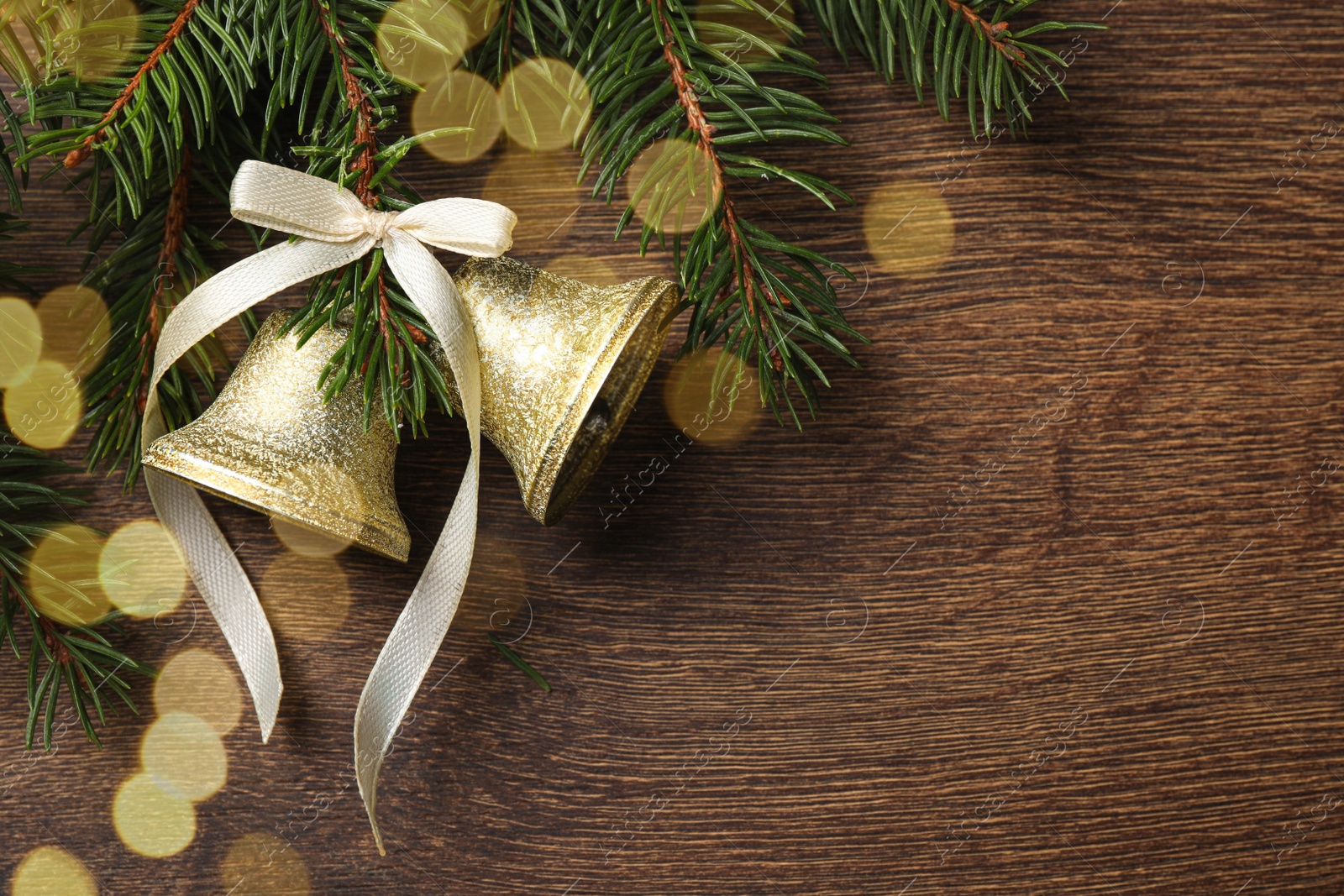 Photo of Christmas bells and fir tree branches on wooden table, flat lay. Space for text