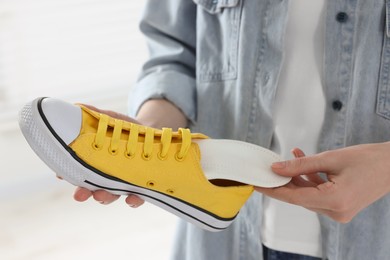 Woman putting orthopedic insole into shoe on blurred background, closeup. Foot care
