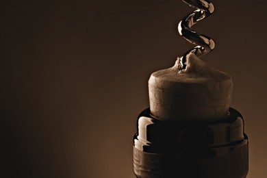 Image of Opening wine bottle with corkscrew on dark brown background, closeup. Space for text