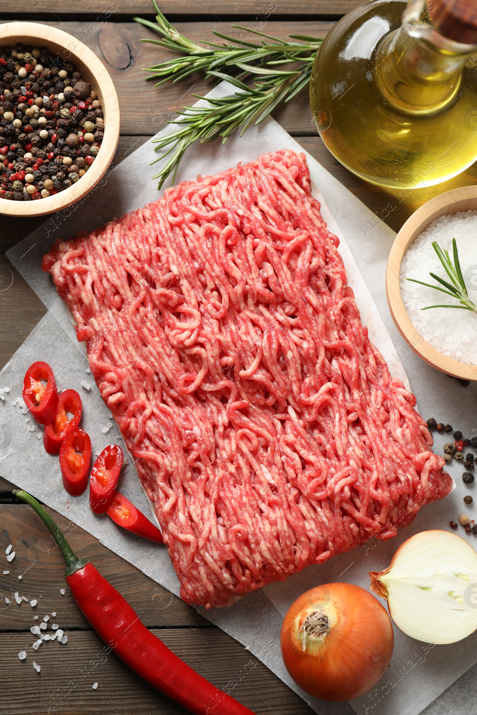 Photo of Raw ground meat, spices, rosemary, oil and onion on wooden table, flat lay