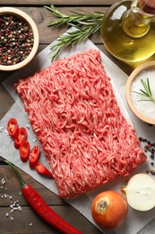 Raw ground meat, spices, rosemary, oil and onion on wooden table, flat lay