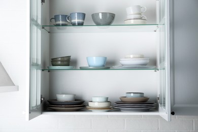 Photo of Open cabinet with different clean plates and bowls in kitchen