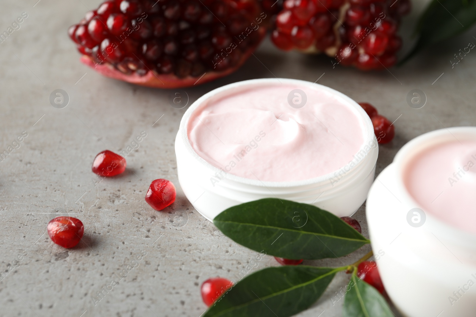 Photo of Natural facial mask, pomegranate seeds and green leaves on light grey table, closeup