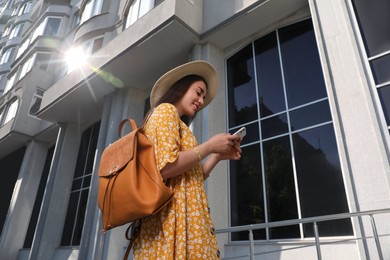 Beautiful young woman with stylish backpack and smartphone outdoors on sunny day, low angle view