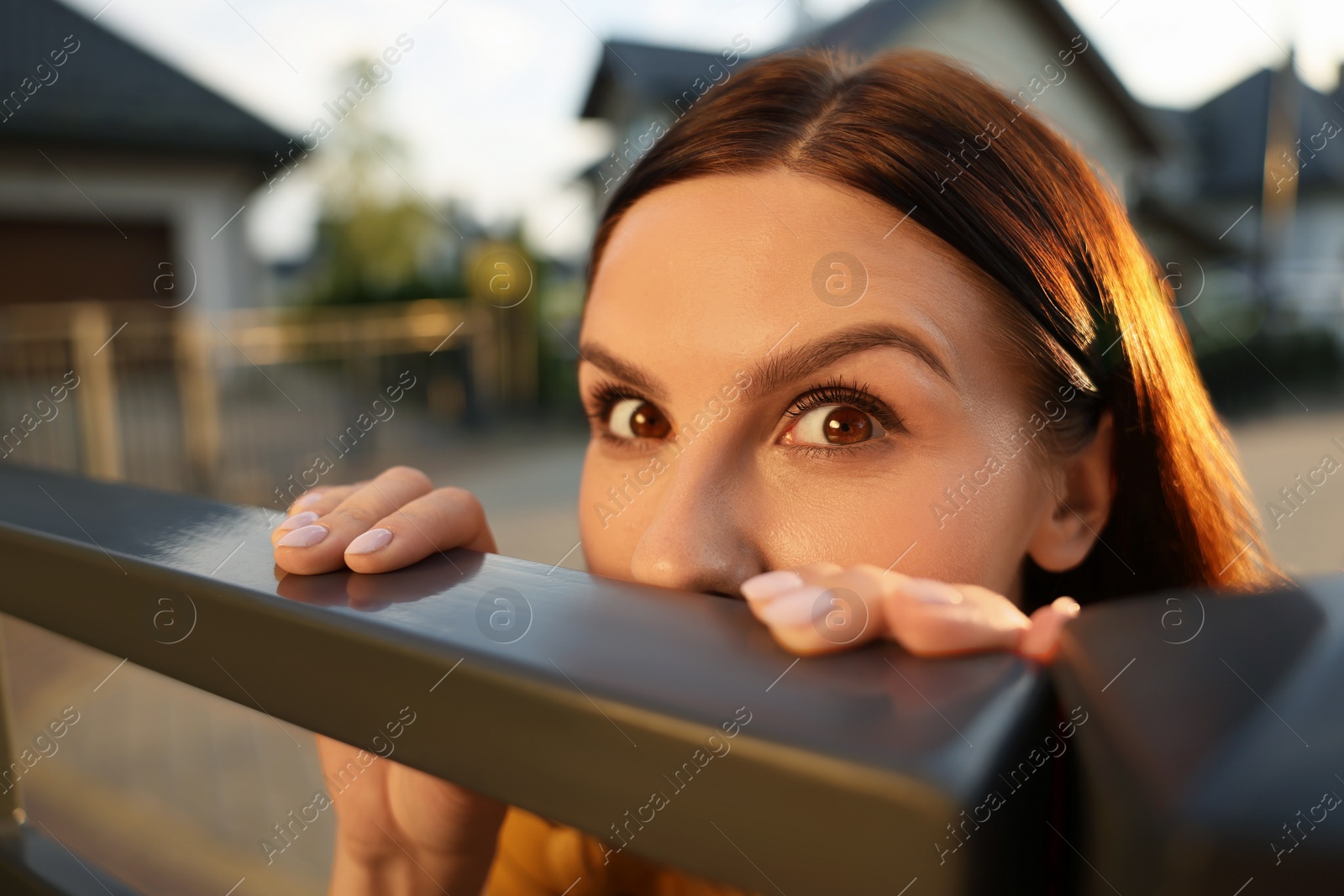 Photo of Concept of private life. Curious young woman spying on neighbours over fence outdoors, closeup