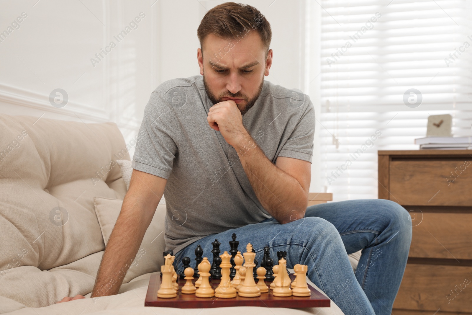 Photo of Thoughtful young man playing chess alone on sofa at home