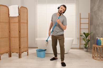 Photo of Happy man with mop singing while cleaning in bathroom