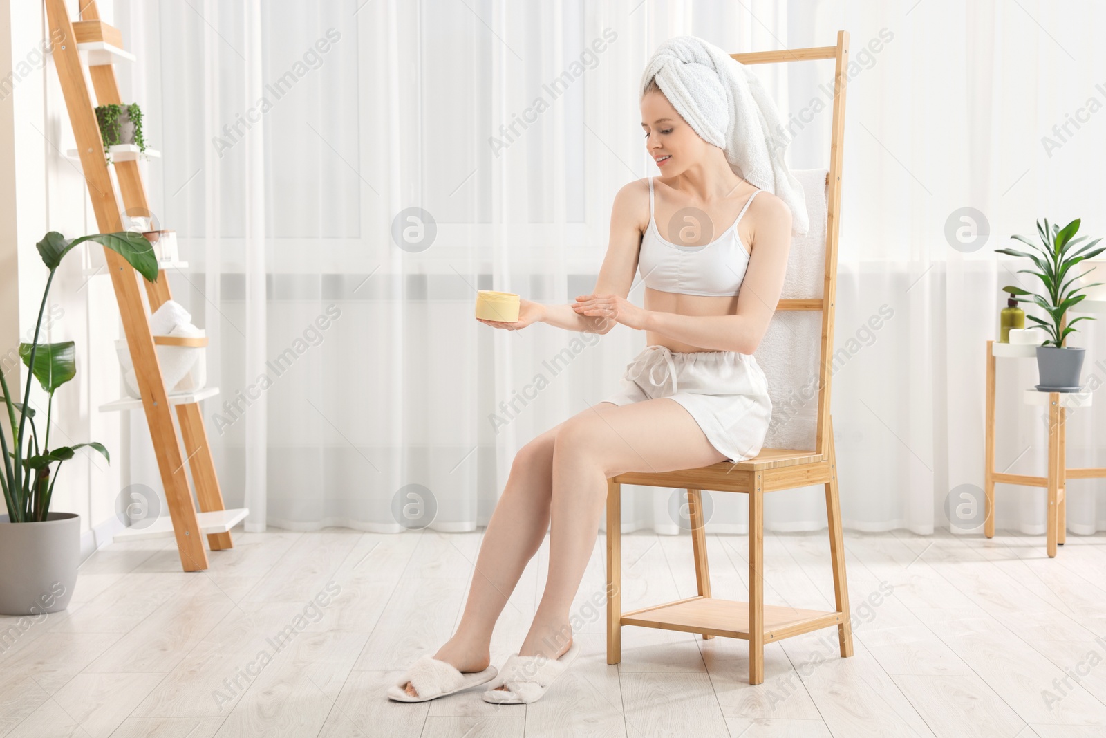 Photo of Beautiful young woman applying body cream onto arm indoors