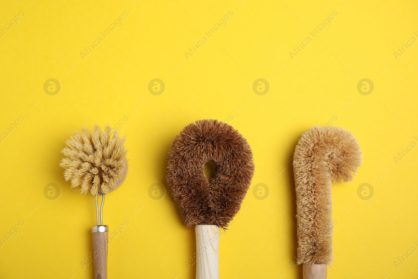 Photo of Cleaning brushes for dish washing on yellow background, flat lay