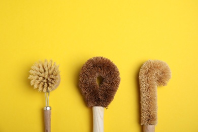Photo of Cleaning brushes for dish washing on yellow background, flat lay