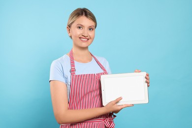 Photo of Beautiful young woman in clean striped apron with tablet on light blue background