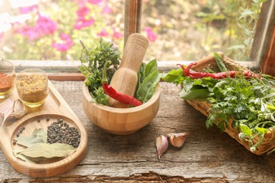 Photo of Mortar with pestle, fresh green herbs and different spices on wooden table near window