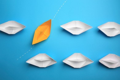 Yellow paper boat floating through others on light blue background, flat lay. Uniqueness concept