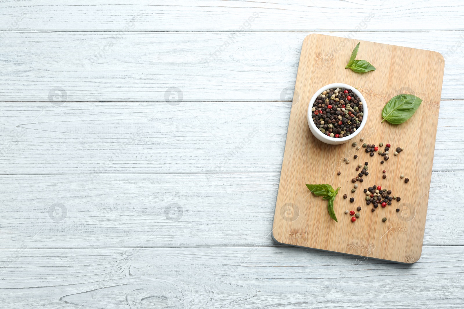 Photo of Wooden board with mixed pepper corns and basil leaves on white table, top view. Space for text