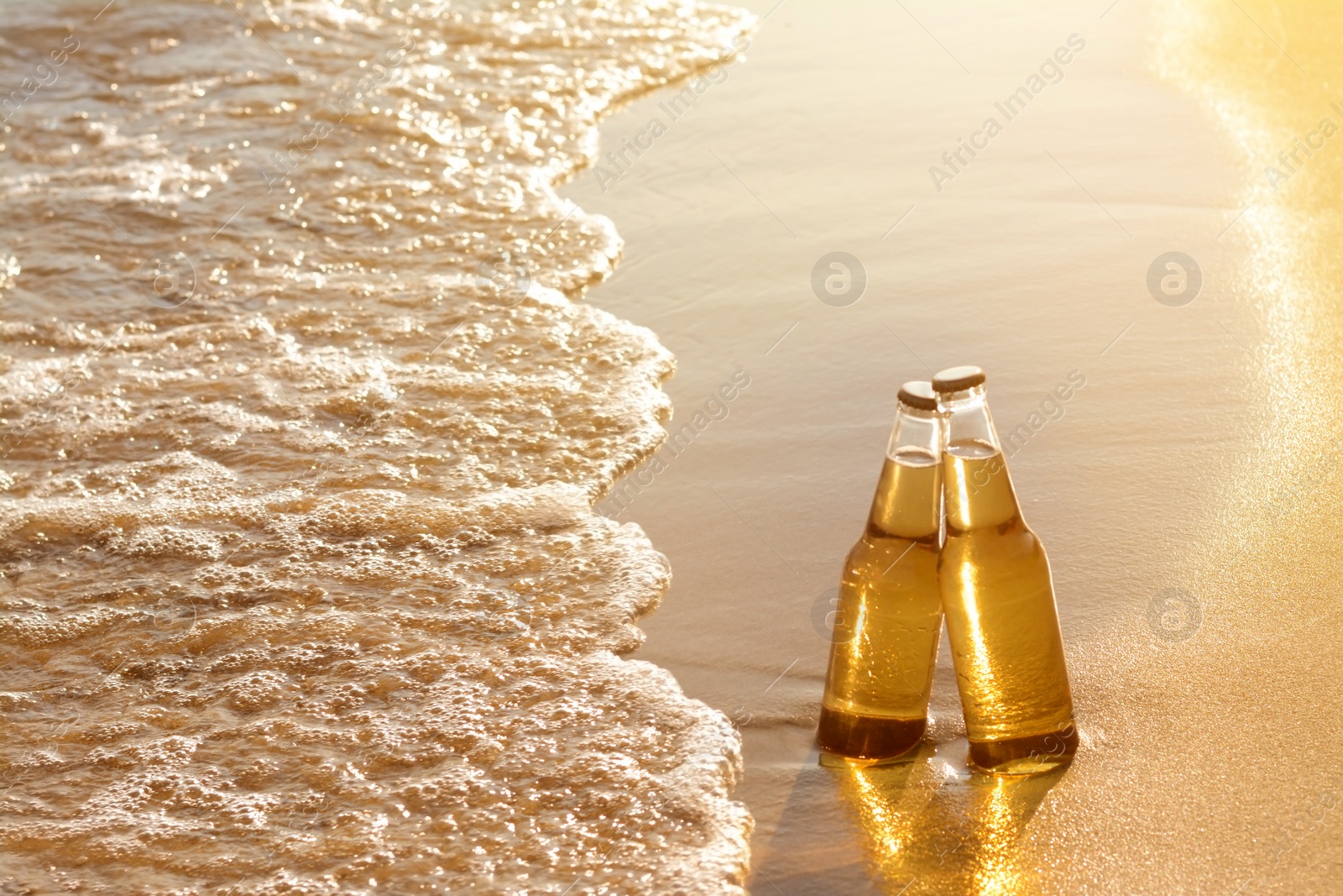 Photo of Bottles of cold beer on sandy beach near sea, space for text