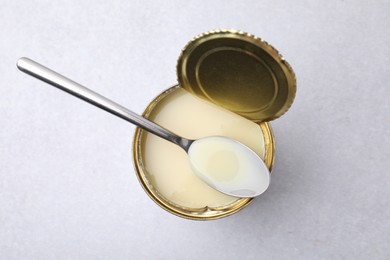 Photo of Open tin can with condensed milk and spoon on white table, top view