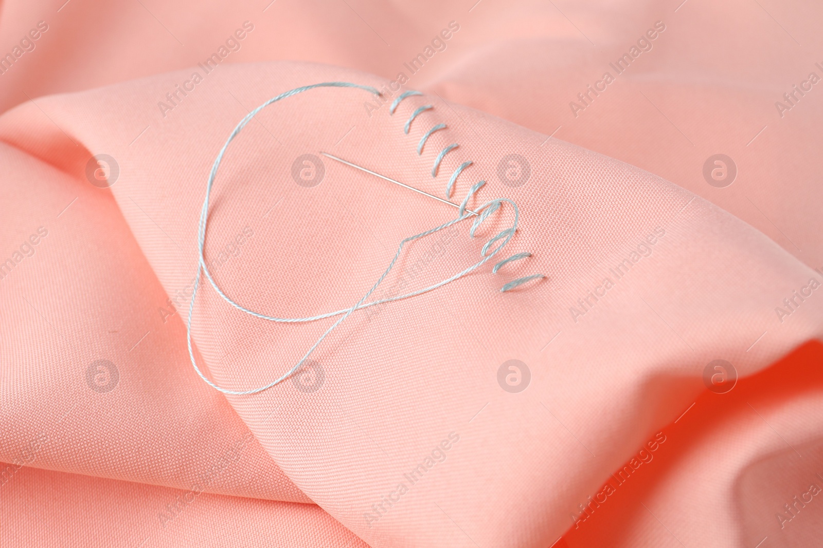 Photo of Sewing needle with thread and stitches on coral cloth, closeup