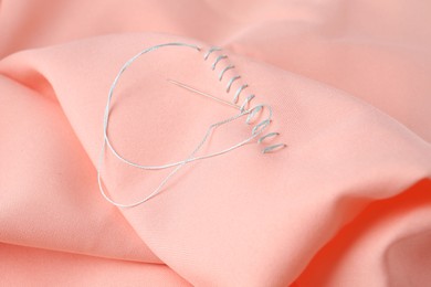 Sewing needle with thread and stitches on coral cloth, closeup