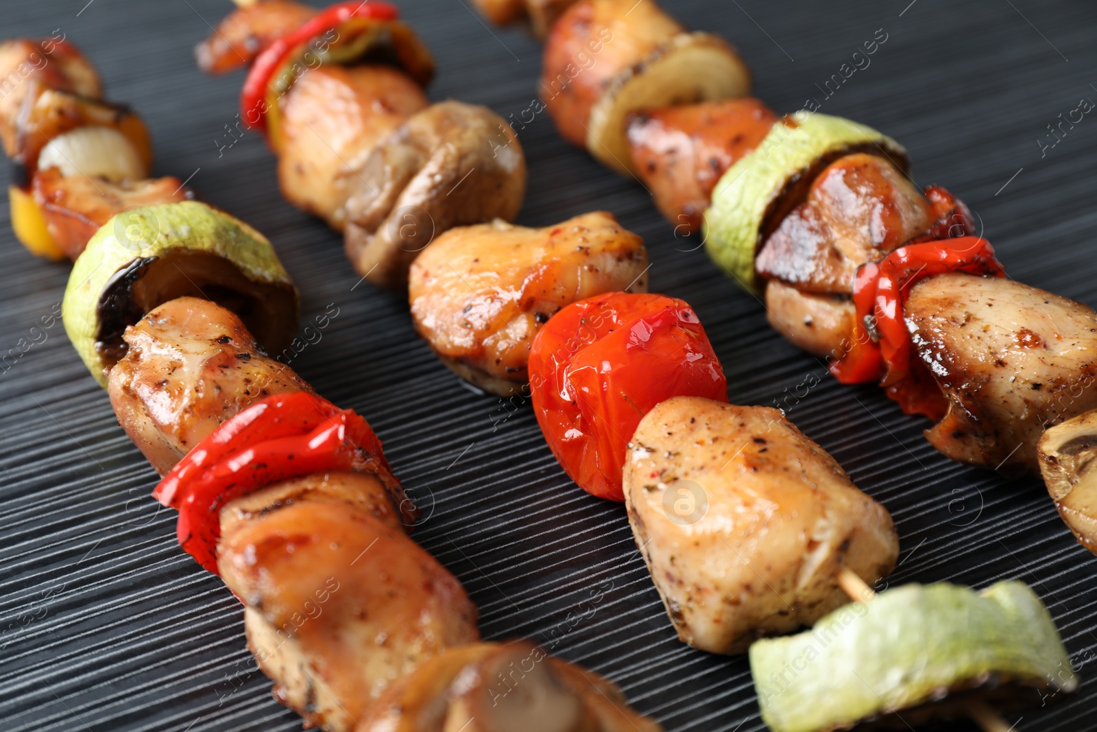 Photo of Delicious shish kebabs with vegetables on black table, closeup