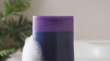 Photo of Purple bottle of bubble bath with foam indoors, closeup