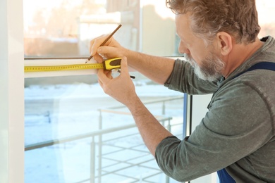 Photo of Service man measuring window for installation indoors