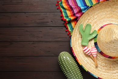 Mexican sombrero hat, maracas, toy cacti and colorful poncho on wooden background, flat lay. Space for text