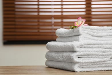 Photo of Stack of clean towels with flower on table indoors. Space for text