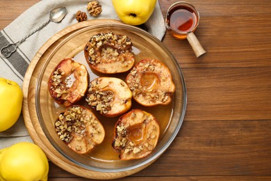 Photo of Tasty baked quinces with walnuts and honey in bowl on wooden table, flat lay. Space for text