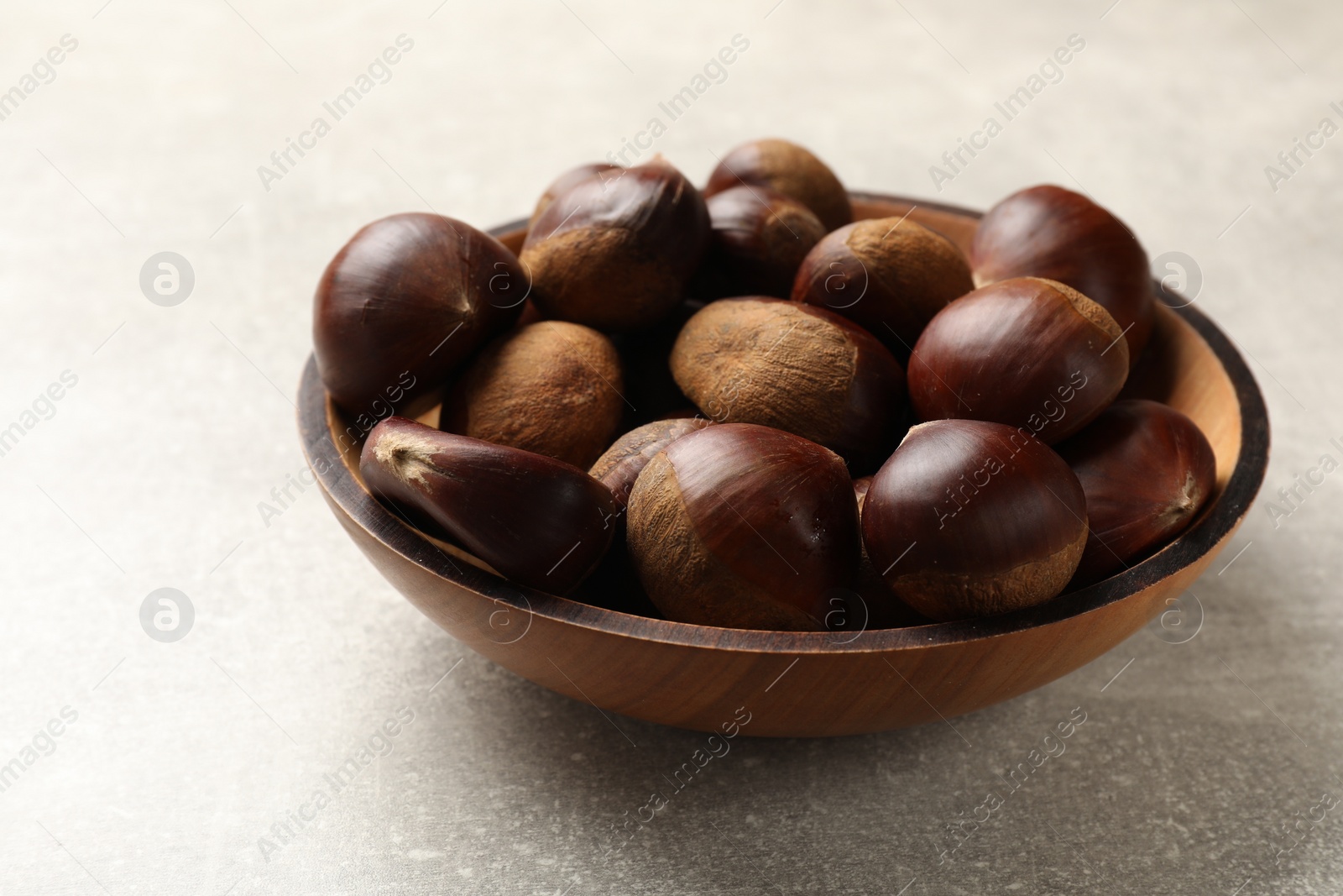 Photo of Roasted edible sweet chestnuts in bowl on light grey table, closeup