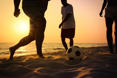 Friends playing football on beach at sunset, closeup