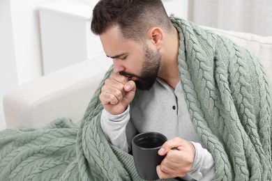 Photo of Sick man with cup coughing at home