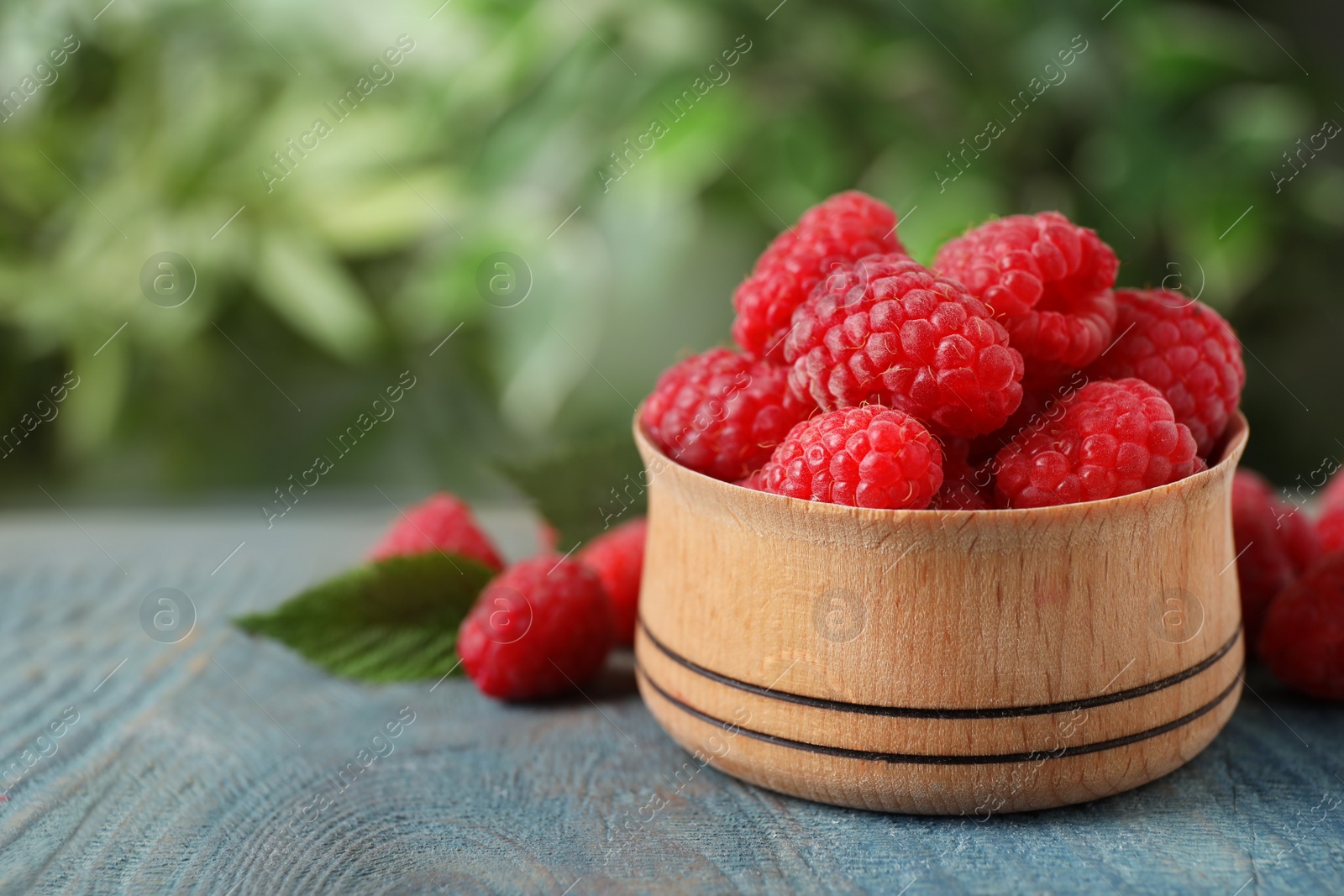 Photo of Delicious fresh ripe raspberries in bowl on blue wooden table