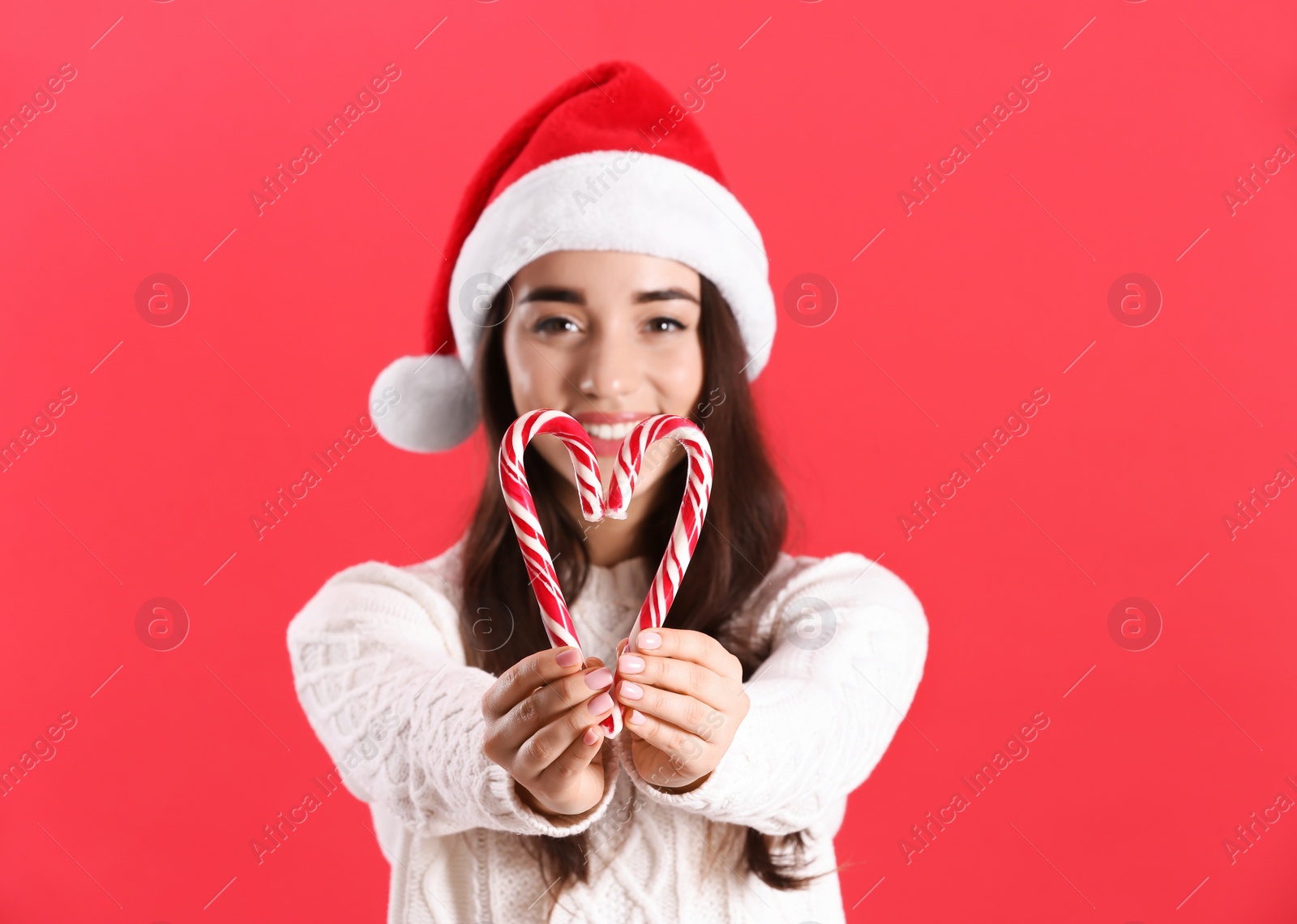 Photo of Beautiful woman in Santa Claus hat making heart with candy canes on red background