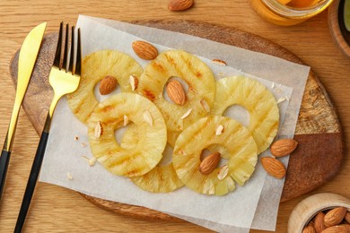 Photo of Tasty grilled pineapple slices and almonds served on wooden table, flat lay
